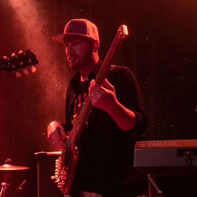 Musician playing an electric bass guitar on stage under red lighting during a live performance.