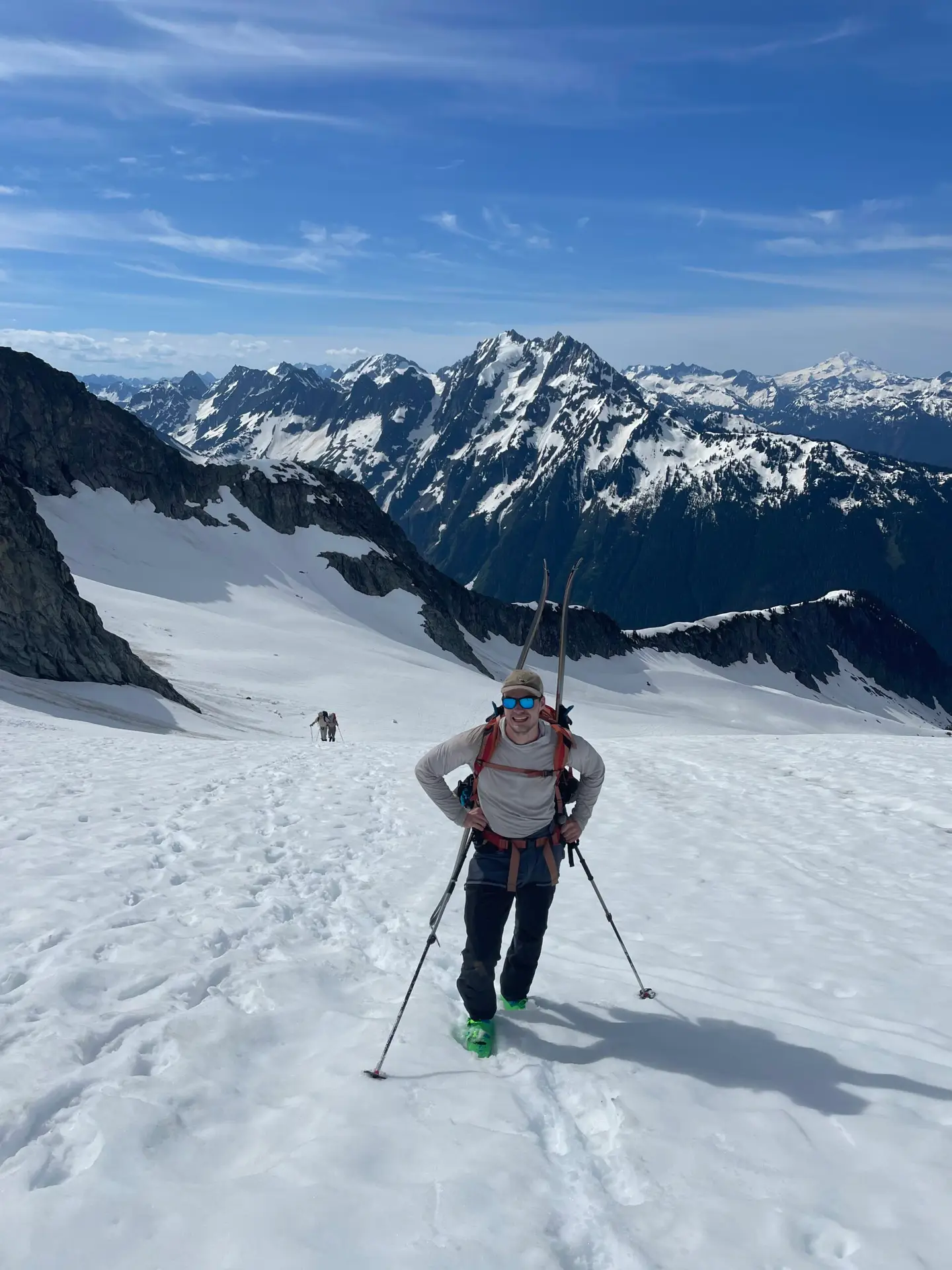 Skier wearing a backpack and skis hiking uphill across a snowfield in the mountains.